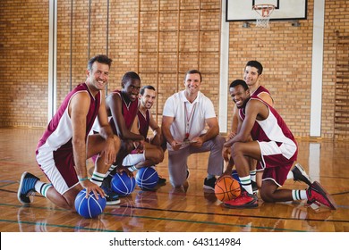 Portrait Of Smiling Coach And Players Kneeling With Basketball In The Court