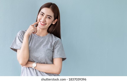 Portrait of smiling confident asian woman in causal t-shirt. Asian friendly girl. Beautiful happy white teeth femal point her cheek  looking camera with copy space isolated on gray
