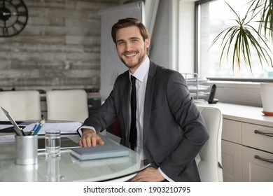 Portrait smiling confident businessman employee worker wearing suit sitting at table in modern office, successful executive leader ceo looking at camera, posing for corporate photo at work desk