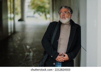 Portrait Of A Smiling And Confident Mature Businessman Walking Outside While Going To A Meeting. Senior Bearded Man Dressed In Stylish Black Coat Standing Outside And Leaning To A Wall. Copy Space.