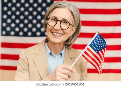 Portrait of smiling confident senior woman, politician holding American flag looking at camera. Vote, United States presidential election concept - Powered by Shutterstock