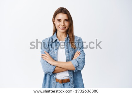 Portrait of smiling confident woman feeling ready and determined, cross arms on chest self-assured looking at camera, standing against white background
