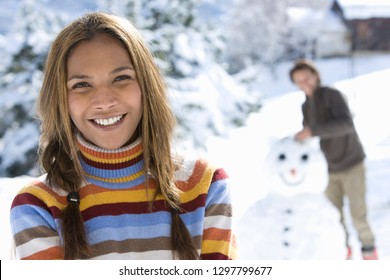 Portrait Of Smiling Couple Building Snowman On Winter Vacation