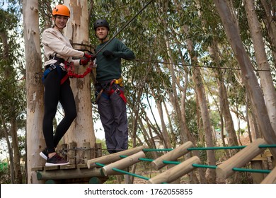 Portrait Of Smiling Couple Holding Zip Line Cable Standing On Wooden Platform In The Forest