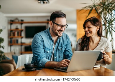 Portrait of a smiling couple at home, relaxing and using laptop.