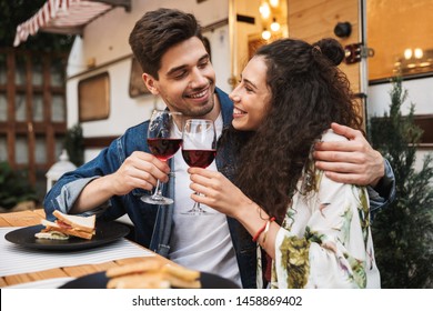 Portrait Of Smiling Couple Man And Woman Drinking Red Wine While Hugging Together At Wooden Table Near Trailer Outdoors