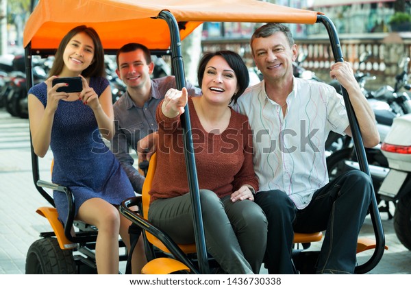 Portrait of smiling couples driving grand tour\
electric outside and making\
photos