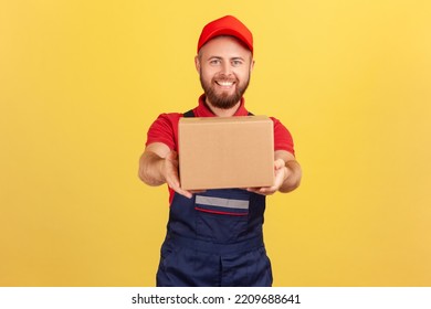 Portrait Of Smiling Courier Man Holding Cardboard Parcel, Delivering Order Door-to-door, Shipment And Cargo Transportation Service. Indoor Studio Shot Isolated On Yellow Background.