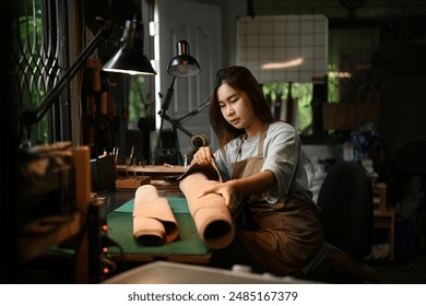 Portrait of a smiling craftswoman wearing an apron working on leather fabric at her workshop. - Powered by Shutterstock