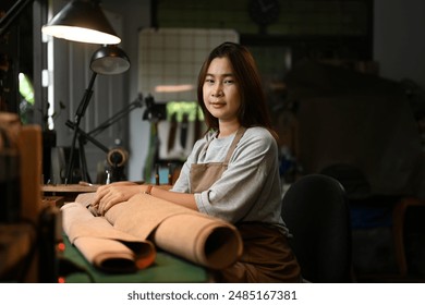 Portrait of a smiling craftswoman wearing an apron working on leather fabric at her workshop. - Powered by Shutterstock