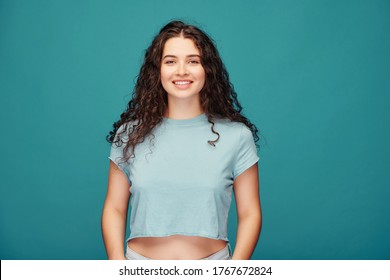 Portrait of smiling curly-haired girl in crop top standing against blue background