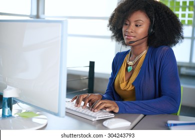 Portrait of a smiling customer service representative with an afro at the computer using headset