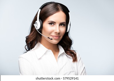 Portrait of smiling customer support female phone worker, against grey background. Consulting and assistance service call center.