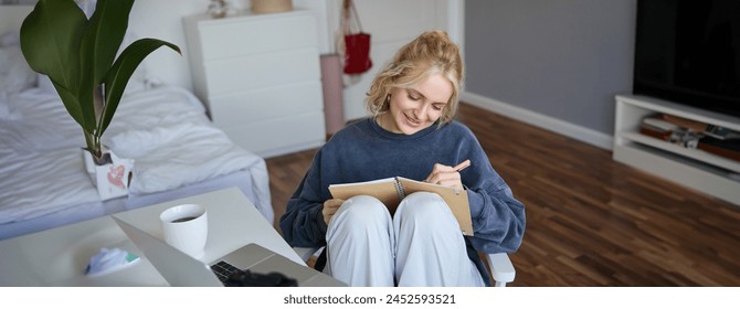 Portrait of smiling cute woman, lifestyle blogger, sits in her room with daily journal or planner, records video on digital camera, creates content for social media about daily routine. - Powered by Shutterstock