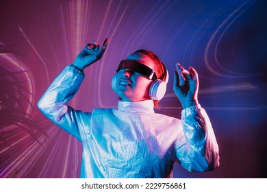 Portrait of a smiling dancing woman in futuristic sunglasses and headphones in pink and blue neon light. Music lover. Silent disco. Woman on the background of music vibes background. Futuristic Party.
