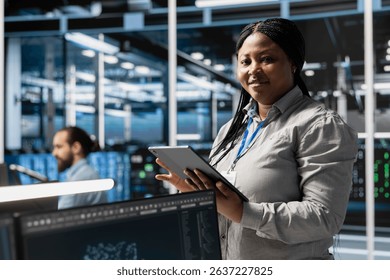 Portrait of smiling data center programmer using tablet to update servers tech, configuring gear using software tools. Happy server farm worker reviewing hardware analytics using device