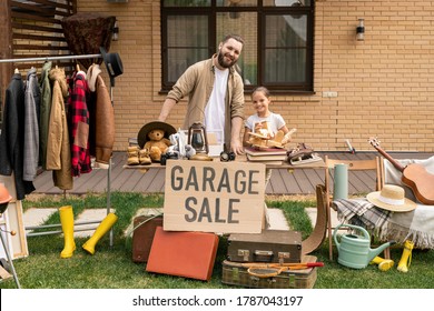 Portrait Of Smiling Daughter Assisting Bearded Father To Sell Old Things At Garage Sale In Backyard