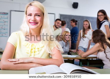 Portrait of smiling diligent female student sitting at her desk alone in college or highschool classroom