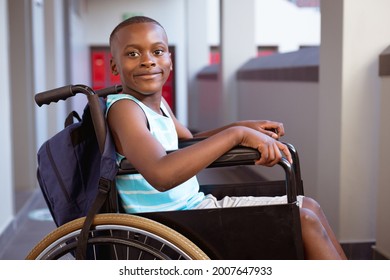 Portrait of smiling disabled african american schoolboy sitting in wheelchair in school corridor. childhood and education at elementary school.