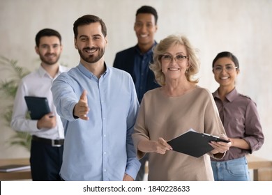 Portrait Of Smiling Diverse Businesspeople Pose At Workplace Stretch Hand For Handshake Get Acquainted Greeting. Happy Multiracial Employees Meet Welcome Newcomer Newbie To Team. Employment Concept.