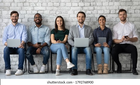 Portrait smiling diverse candidates sitting on chairs in row, looking at camera, business people applicants interns waiting for job interview, holding gadgets, employments and recruitment concept - Shutterstock ID 1792768900