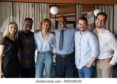 Portrait Of Smiling Diverse Employees Colleagues Team Hugging Standing In Office, Happy Successful Businesspeople Partners Looking At Camera, Workers Group Posing For Photo, Unity And Cooperation