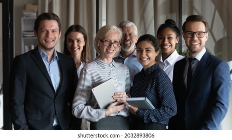 Portrait Of Smiling Diverse Employees Workers With Mature Team Leader Executive Standing In Office, Looking At Camera, Happy Business Partners Colleagues Coworkers Posing For Corporate Photo