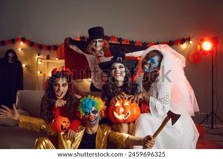 Portrait of smiling diverse young people in scary horror costumes celebrate Halloween in decorated home together. Happy multiethnic friends on masquerade enjoy all saint eve party celebration.