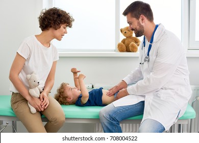 Portrait of smiling doctor examining stomach of little boy and asking him to say where it hurts