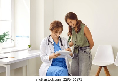 Portrait of smiling doctor wearing stethoscope holding report file with appointment and giving consultation to girl patient. Happy teenage is listening to doctor during medical examination in clinic. - Powered by Shutterstock