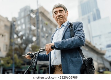 Portrait of smiling elderly businessman riding a bicycle downtown - Powered by Shutterstock