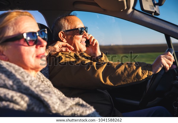 Portrait of smiling elderly couple driving car,\
while driver talking on\
phone.