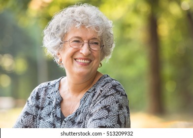 Portrait of smiling elderly woman with eyeglasses at park. Laughing senior woman looking away. Happy thoughful mature woman relaxing outdoor. Old active retired woman.