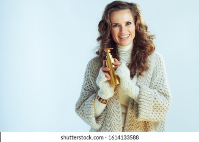 Portrait Of Smiling Elegant 40 Year Old Woman With Long Wavy Hair In Neck Sweater And Cardigan With Self Tanning Lotion Isolated On Winter Light Blue.