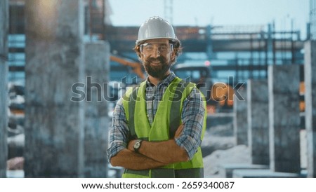 Portrait of a smiling engineer posing with crossed arms at construction site, wearing safety helmet and vest