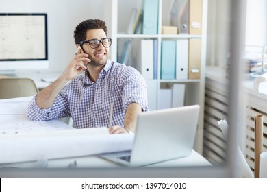 Portrait of smiling engineer speaking by phone at workplace in office, copy space