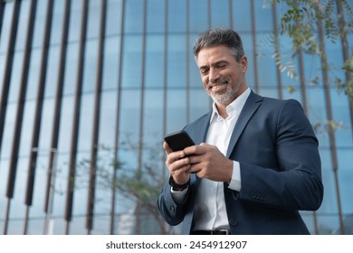 Portrait of smiling executive ceo manager. Latin adult man in suit using smartphone application app device for business at office outdoors. Successful mid age senior businessman holding mobile phone. 