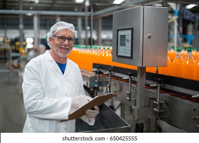 Portrait of smiling factory engineer maintaining record on clipboard in drinks production plant - Powered by Shutterstock