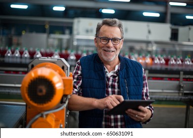 Portrait of smiling factory worker standing with a digital tablet in drinks production plant - Powered by Shutterstock