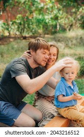 Portrait Of Smiling Family With Child Outdoors. Mid Adult Couple Sitting At Sandpit, Father Patting Head Of His Daughter. Family And Childcare Concept