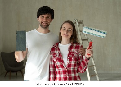 Portrait Smiling Family Couple Holding Paint Roller And Brush. Young Couple Doing Home Repairs