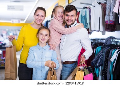 Portrait Of Smiling Family Of Four With Shopping Bags In Clothing Shop