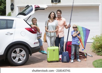 Portrait Of Smiling Family Packing Car In Sunny Driveway