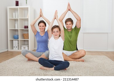 Portrait Of Smiling Family Practicing Yoga On Rug At Home