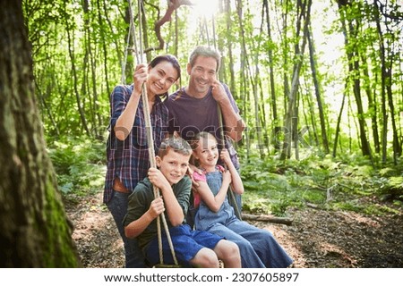 Portrait smiling family at rope swing in woods