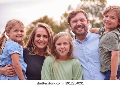 Portrait Of Smiling Family In Summer Garden With Parents Holding Son And Daughter In Arms