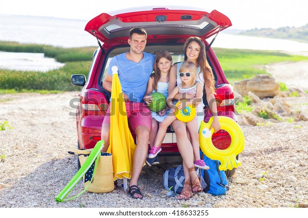 Portrait of a smiling family with two\
children at beach by car. Holiday and travel\
concept