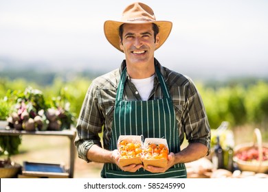 Portrait Of A Smiling Farmer Holding Box Of Fruit At Local Market