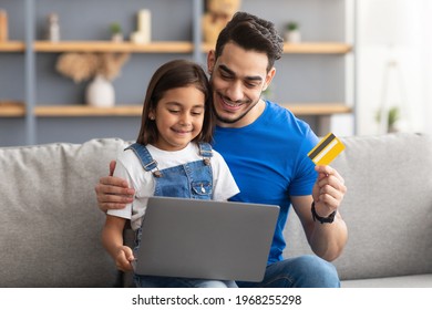 Portrait Of Smiling Father And Kid Shopping Together On Internet, Using Laptop And Credit Card, Sitting And Hugging On Couch At Home, Looking At Computer Screen And Smiling, Order Food, Copy Space