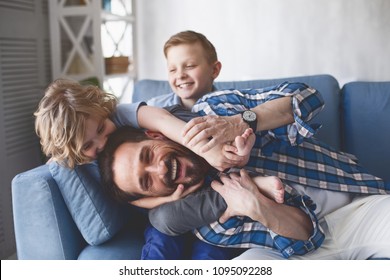 Portrait Of Smiling Father And Outgoing Sons Having Fun On Cozy Couch In Apartment. Happy Family Concept